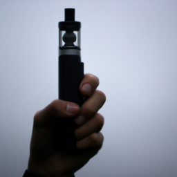 description: An anonymous person holding a vape device in their hand, with a cloud of vapor visible in the background.