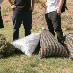 A group of people standing in a grassy area with multiple large bags of cannabis on the ground in front of them.